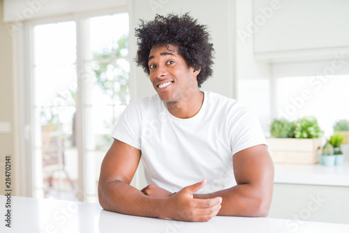 Young african american man wearing casual white t-shirt sitting at home smiling looking to the side and staring away thinking.