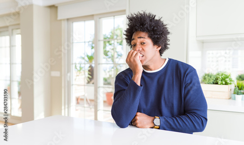 Young african american man wearing casual sweater sitting at home looking stressed and nervous with hands on mouth biting nails. Anxiety problem. © Krakenimages.com