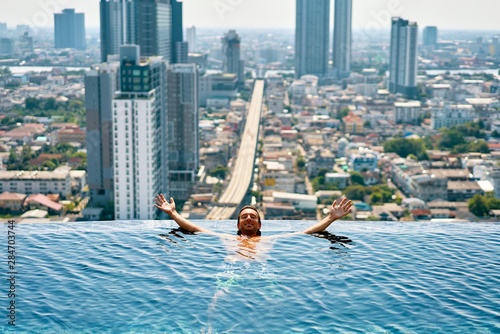 Photography Young happy man relax on the edge of swimming pool in roof top of hotel