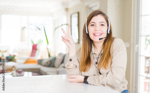 Beautiful young operator woman wearing headset at the office smiling with happy face winking at the camera doing victory sign. Number two.