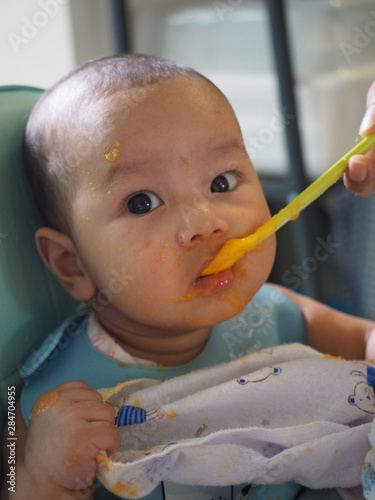 Asian cute little baby eating tasty food from spoon at home,Sloppy face