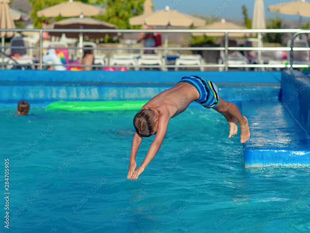 Caucasian boy having fun making fantastic jump into swimming pool at resort.  He is enjoying his summer vacations.