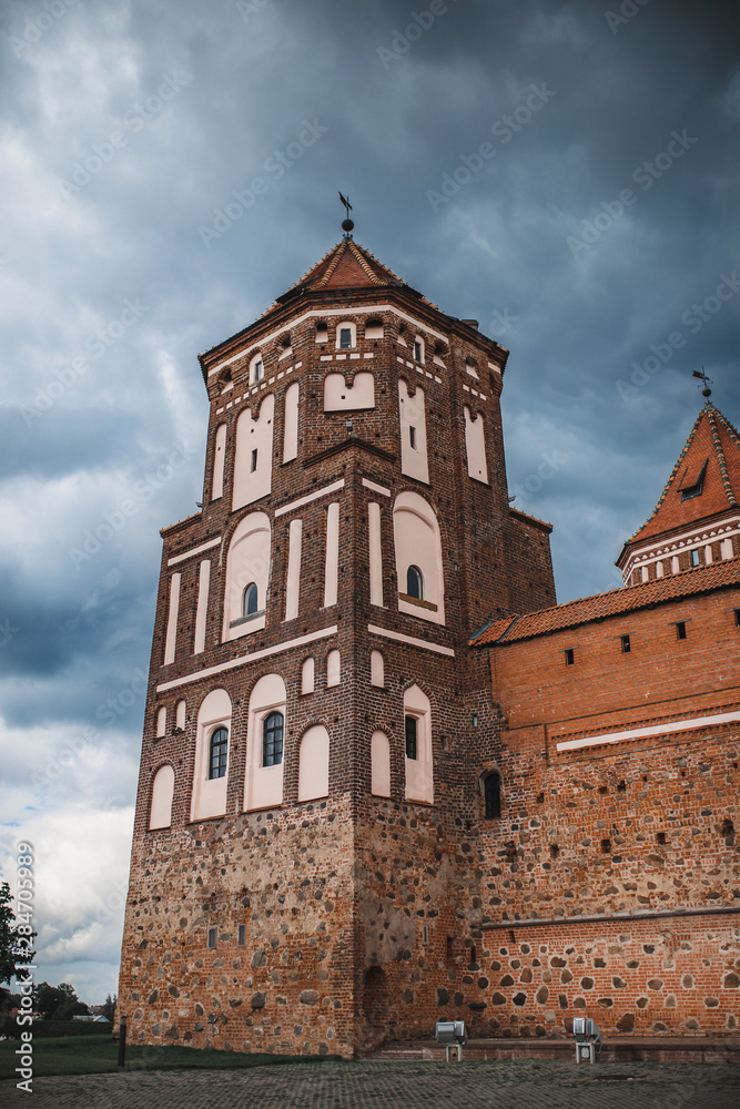 Mysterious medieval red brick castle with tiled roof in cloudy weather with ominous clouds in the sky