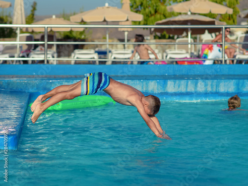 Caucasian boy spending time in pool at resort. He is making high jump to dive into swimming pool.