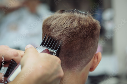 Barber is cutting a hair to Caucasian boy in barbershop.