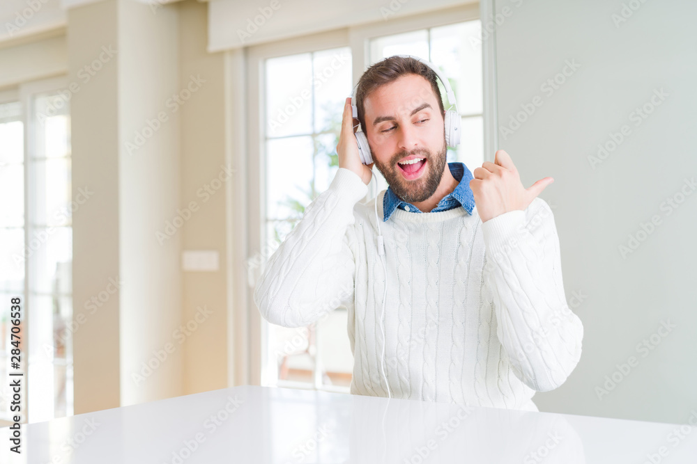 Handsome man wearing headphones and listening to music pointing and showing with thumb up to the side with happy face smiling