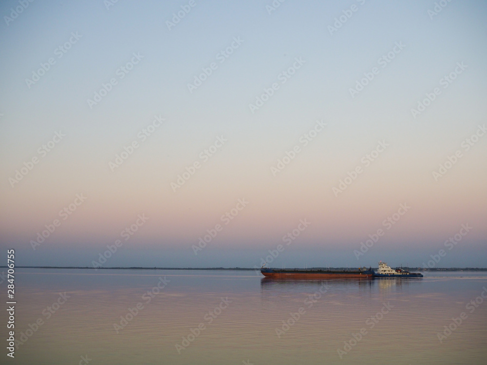 large barge floats on a smooth river at sunset