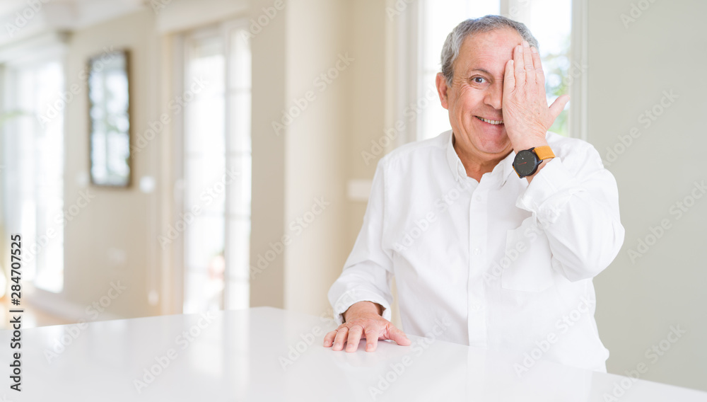 Handsome senior man at home covering one eye with hand with confident smile on face and surprise emotion. Handsome senior man at home covering one eye with hand with confident smile on face and surprise emotion.