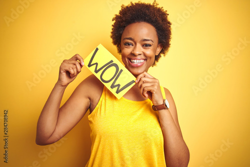 Young african american woman showing wow banner board over yellow isolated background with a happy face standing and smiling with a confident smile showing teeth