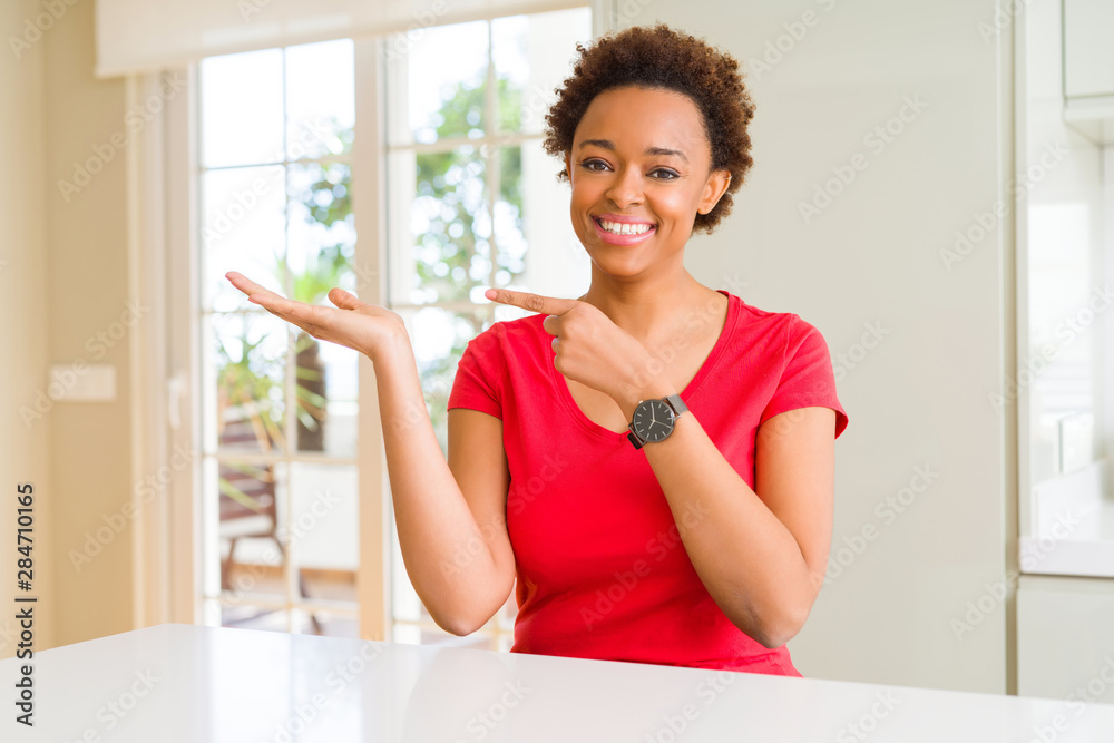Young beautiful african american woman at home amazed and smiling to the camera while presenting with hand and pointing with finger.