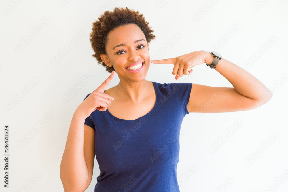Young beautiful african american woman over white background smiling confident showing and pointing with fingers teeth and mouth. Health concept.