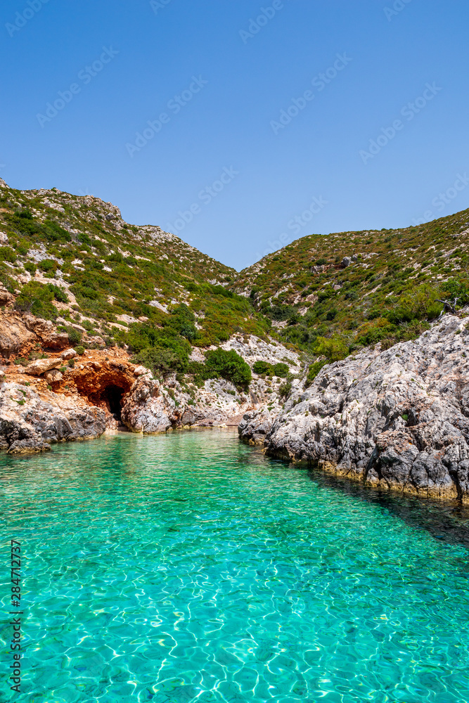Small, paradisiacal bay of Porto Limnionas with view over the clear, turquoise water and rocks covered with bushes, Zakynthos, Greece
