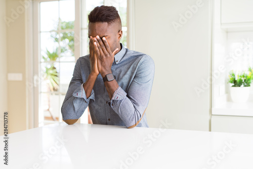 Handsome african american man on white table with sad expression covering face with hands while crying. Depression concept.