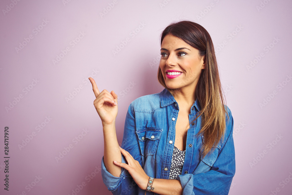 Young beautiful woman standing over pink isolated background with a big smile on face, pointing with hand and finger to the side looking at the camera. Young beautiful woman standing over pink isolated background with a big smile on face, pointing with hand and finger to the side looking at the camera.