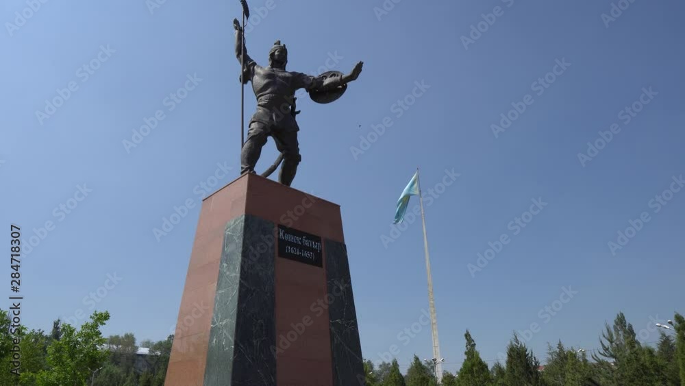 Taraz Presidential Park Statue of Koshek Batyr Holding a Spear with Huge Waving Kazakhstan Flag at Background on a Sunny Blue Sky Day Taraz Presidential Park Statue of Koshek Batyr Holding a Spear with Huge Waving Kazakhstan Flag at Background on a Sunny Blue Sky Day