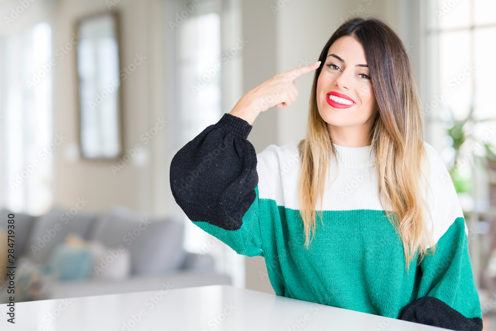 Young beautiful woman wearing winter sweater at home Smiling pointing to head with one finger, great idea or thought, good memory Young beautiful woman wearing winter sweater at home Smiling pointing to head with one finger, great idea or thought, good memory