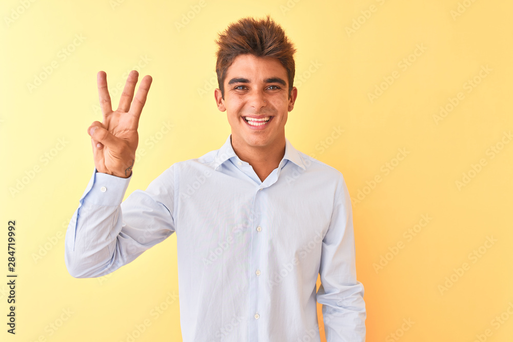 Young handsome businessman wearing elegant shirt over isolated yellow background showing and pointing up with fingers number three while smiling confident and happy.