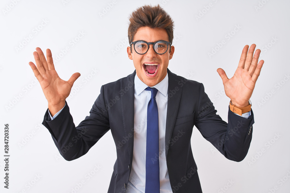 Young handsome businessman wearing suit and glasses over isolated white background celebrating crazy and amazed for success with arms raised and open eyes screaming excited. Winner concept Young handsome businessman wearing suit and glasses over isolated white background celebrating crazy and amazed for success with arms raised and open eyes screaming excited. Winner concept
