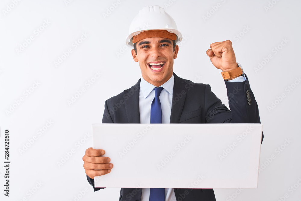 Young handsome architect man wearing helmet holding banner over isolated white background screaming proud and celebrating victory and success very excited, cheering emotion Young handsome architect man wearing helmet holding banner over isolated white background screaming proud and celebrating victory and success very excited, cheering emotion