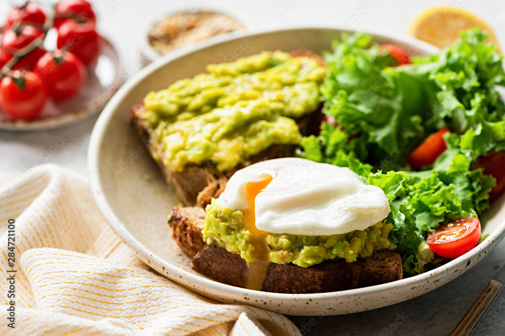 Poached egg on rye toast with avocado and kale tomato salad. Healthy breakfast, lunch. Clean eating concept Poached egg on rye toast with avocado and kale tomato salad. Healthy breakfast, lunch. Clean eating concept