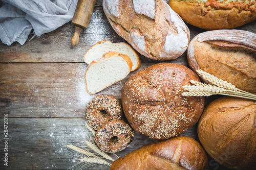 Assortment of fresh baked bread and buns on wooden table background, top view