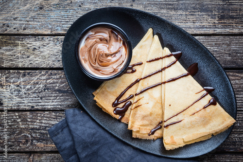 Crepes with chocolate spread. Homemade thin crepes for breakfast or dessert on wooden background, top view. photo