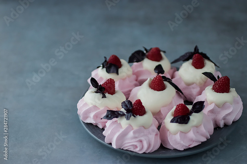 Raspberry meringues with fresh raspberries  basil and whipped cream on a gray plate.