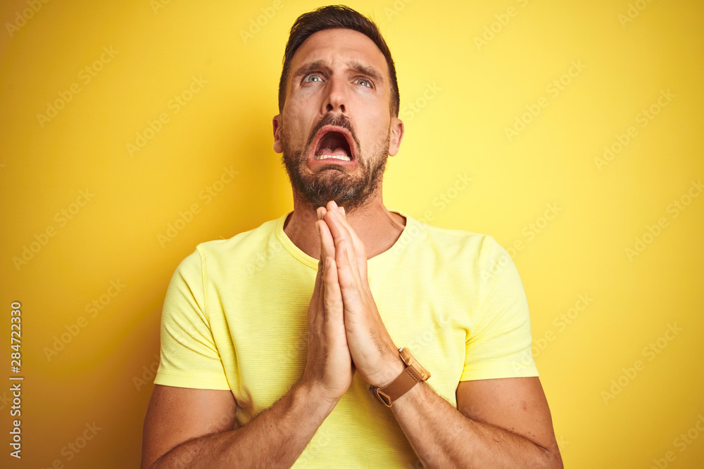 Young handsome man wearing casual yellow t-shirt over yellow isolated background begging and praying with hands together with hope expression on face very emotional and worried. Asking for forgiveness Young handsome man wearing casual yellow t-shirt over yellow isolated background begging and praying with hands together with hope expression on face very emotional and worried. Asking for forgiveness