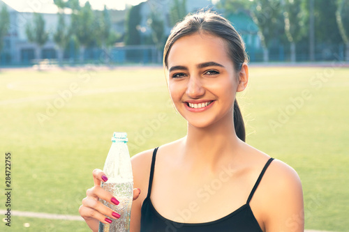 Portrait of an attractive girl with a sports figure drinks water from a bottle.