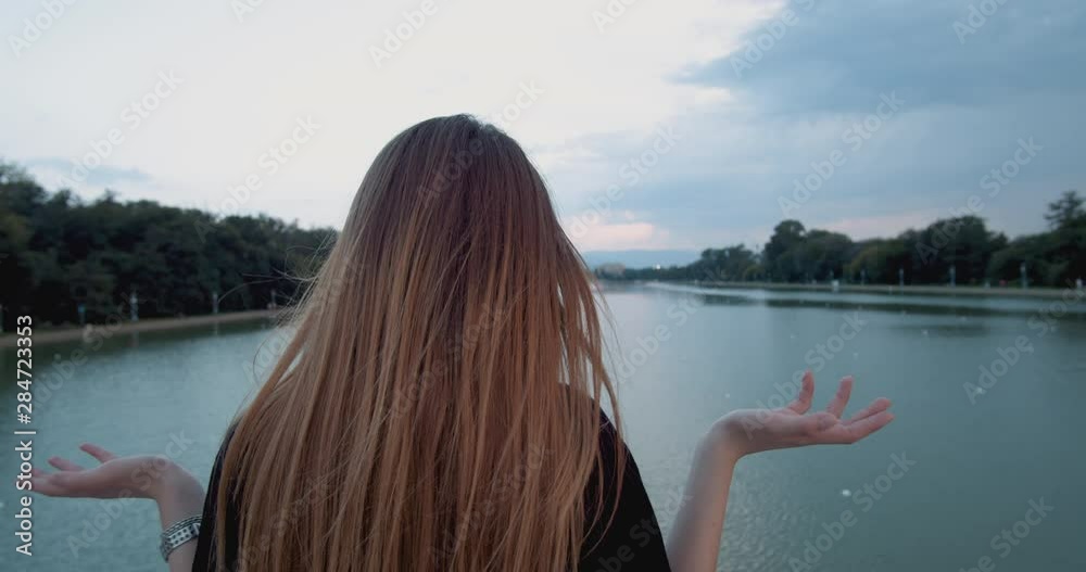 Young woman makes hand gesture that means I don't know, standing on river bridge Young woman makes hand gesture that means I don't know, standing on river bridge