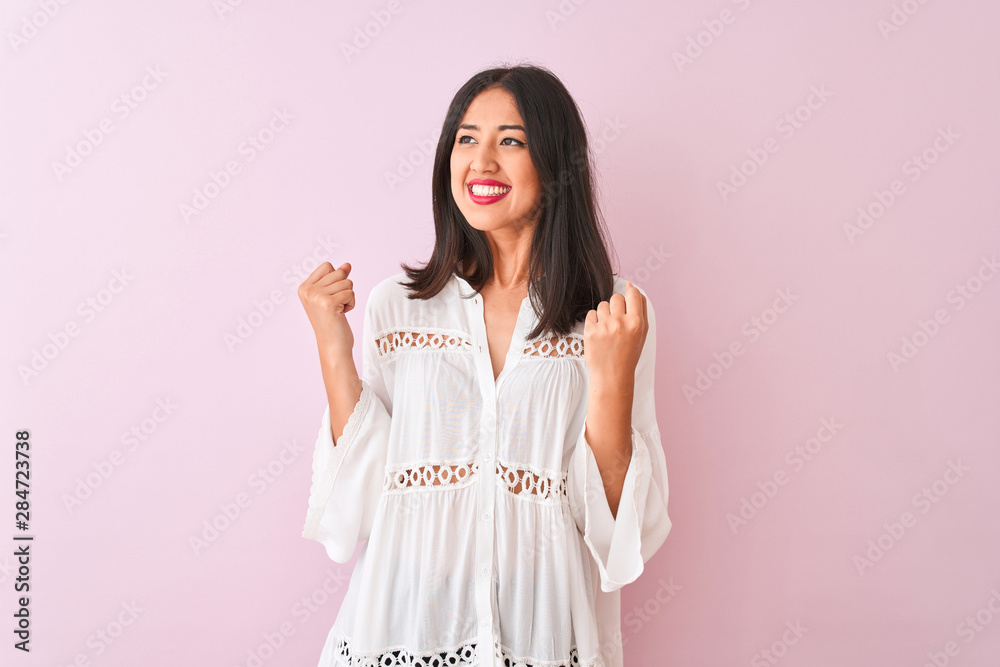 Young chinese woman wearing summer shirt standing over isolated pink background very happy and excited doing winner gesture with arms raised, smiling and screaming for success. Celebration concept. Young chinese woman wearing summer shirt standing over isolated pink background very happy and excited doing winner gesture with arms raised, smiling and screaming for success. Celebration concept.