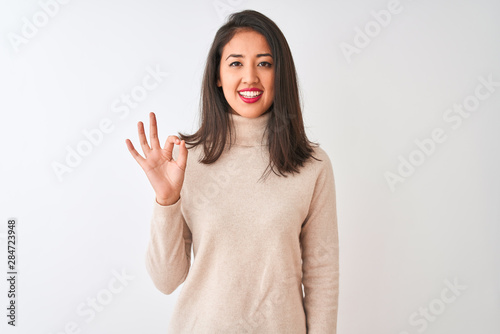 Beautiful chinese woman wearing turtleneck sweater standing over isolated white background smiling positive doing ok sign with hand and fingers. Successful expression.
