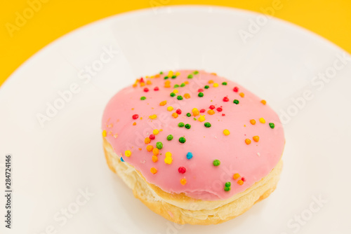 Pink round donut on white plate on yellow  background