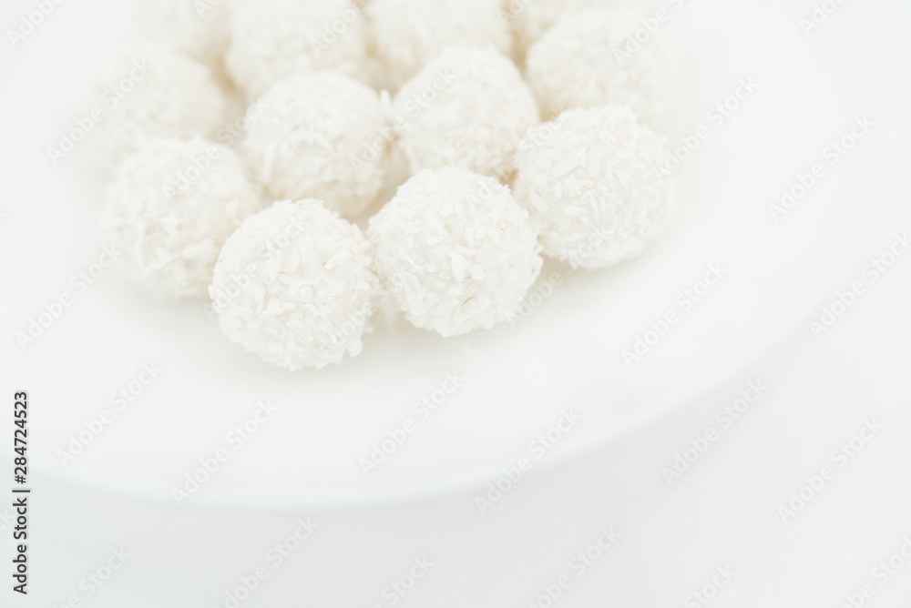 Chocolate covered coconut candies on white plate isolated on white background. Truffle candy set. Selective focus Chocolate covered coconut candies on white plate isolated on white background. Truffle candy set. Selective focus