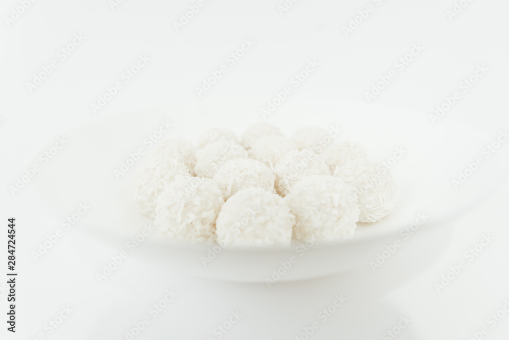 Chocolate covered coconut candies on white plate isolated on white background. Truffle candy set. Selective focus Chocolate covered coconut candies on white plate isolated on white background. Truffle candy set. Selective focus
