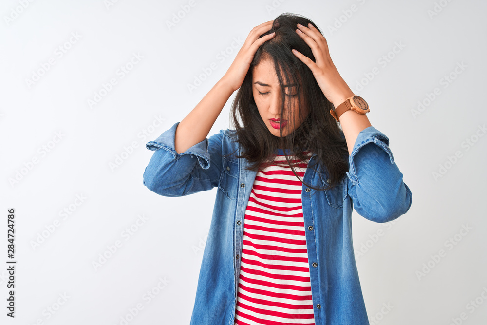 Young chinese woman wearing striped t-shirt and denim shirt over isolated white background suffering from headache desperate and stressed because pain and migraine. Hands on head. Young chinese woman wearing striped t-shirt and denim shirt over isolated white background suffering from headache desperate and stressed because pain and migraine. Hands on head.