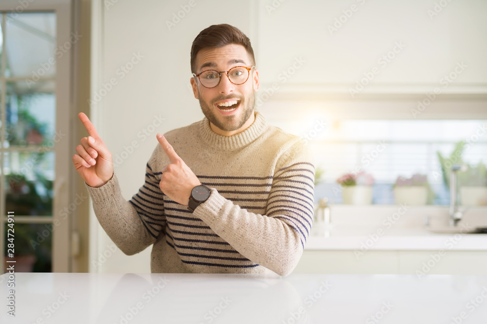 Young handsome man wearing glasses at home smiling and looking at the camera pointing with two hands and fingers to the side. Young handsome man wearing glasses at home smiling and looking at the camera pointing with two hands and fingers to the side.