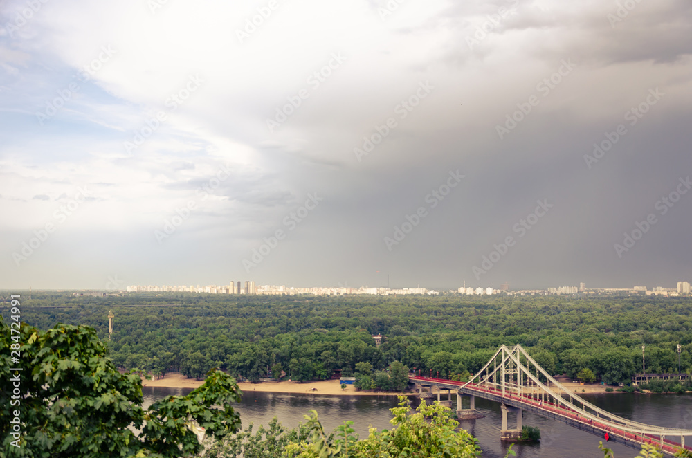 View of pedestrian Park bridge over the Dnipro river. Cloudy sky after rain. Summertime