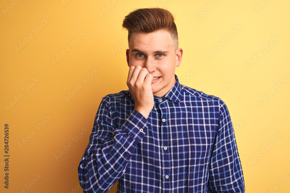 Young handsome man wearing casual shirt standing over isolated yellow background looking stressed and nervous with hands on mouth biting nails. Anxiety problem. Young handsome man wearing casual shirt standing over isolated yellow background looking stressed and nervous with hands on mouth biting nails. Anxiety problem.