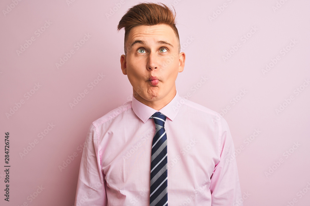 Young handsome businessman wearing shirt and tie standing over isolated pink background making fish face with lips, crazy and comical gesture. Funny expression.