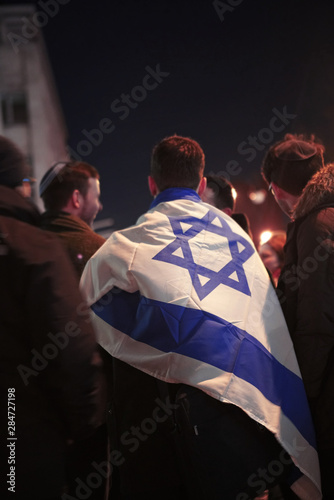 Group of young jewish men gathered at night, with a flag of Israel draped over one of them.