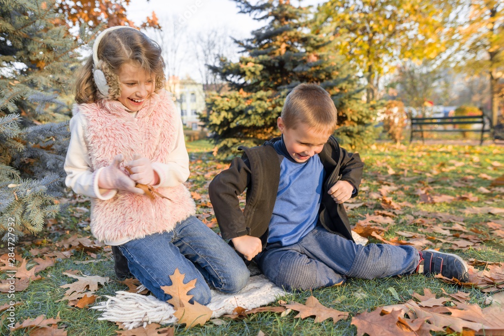 Happy kids playing and sitting on yellow leaves Happy kids playing and sitting on yellow leaves