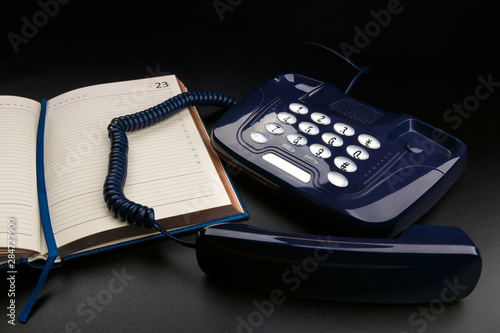 Outdated push-button telephone with handset and personal organizer on black background