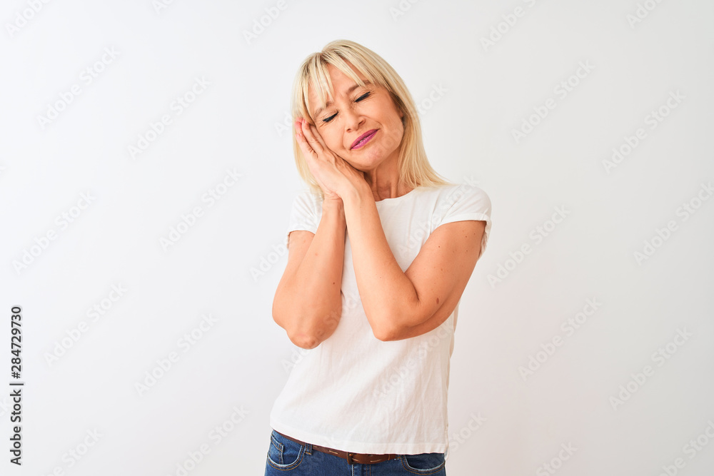 Middle age woman wearing casual t-shirt standing over isolated white background sleeping tired dreaming and posing with hands together while smiling with closed eyes.