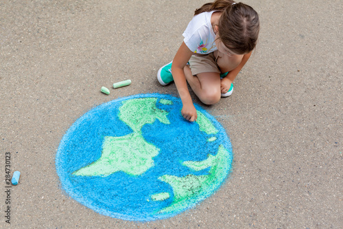 the  child girl draws a planet of the world with colored chalk on the asphalt. Children's drawings, paintings and concepts. Education and art, be creative when you return to school.  earth, Peace day