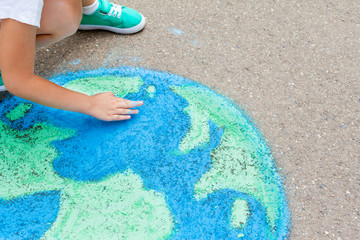 the  child girl draws a planet of the world with colored chalk on the asphalt. Children's drawings, paintings and concepts. Education and art, be creative when you return to school.  earth, Peace day