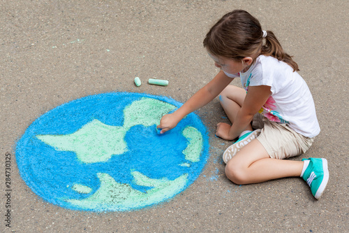 the  child girl draws a planet of the world with colored chalk on the asphalt. Children's drawings, paintings and concepts. Education and art, be creative when you return to school.  earth, Peace day