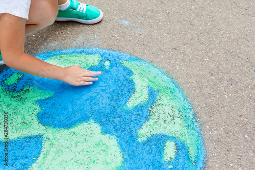 the  child girl draws a planet of the world with colored chalk on the asphalt. Children's drawings, paintings and concepts. Education and art, be creative when you return to school.  earth, Peace day