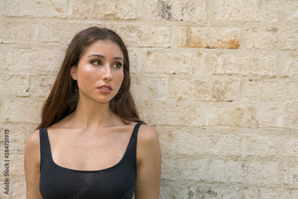 Sexy young woman posing in a black tank top on a brick wall