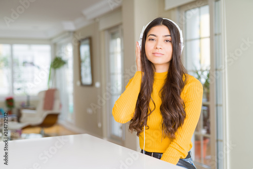 Young woman wearing headphones listening to music with serious expression on face. Simple and natural looking at the camera.